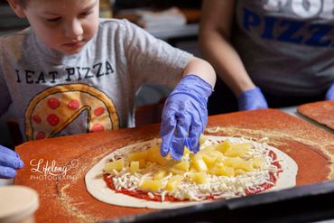 Chef's son adding adding toppings to a pizza. Commercial photo shoot in Snohomish, WA