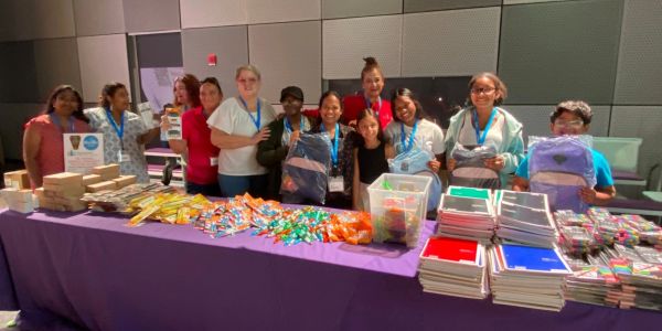 Group of people with school supplies on a table.