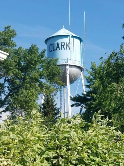 Blue water tower labeled 'CLARK' surrounded by green trees under a clear sky.