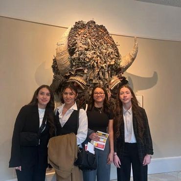 Four women posing in front of a large buffalo head sculpture.