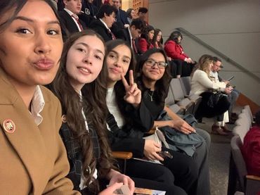 Four young women posing for a selfie in an auditorium.