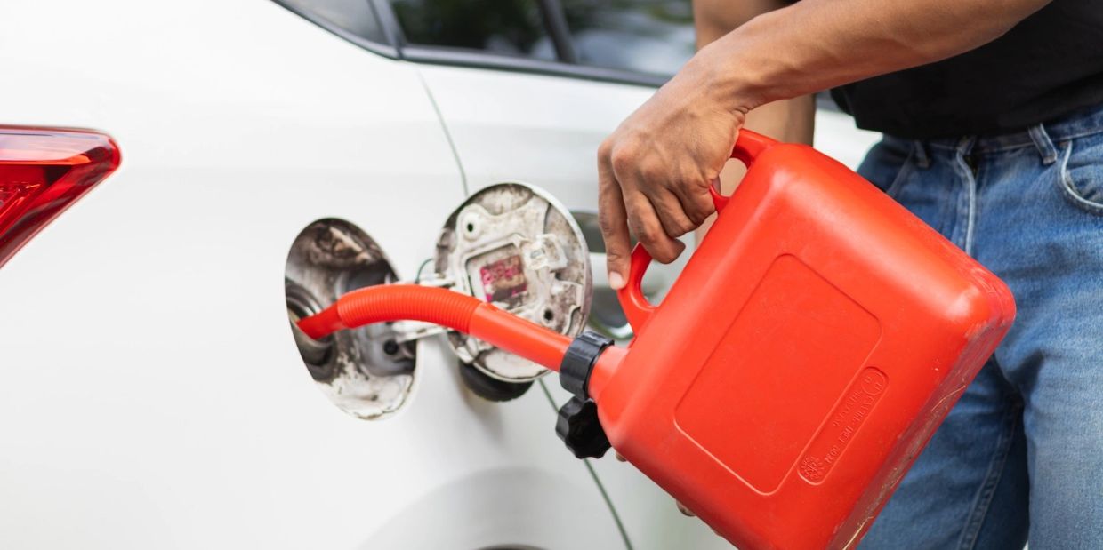Person refueling a white car using a red gasoline container.