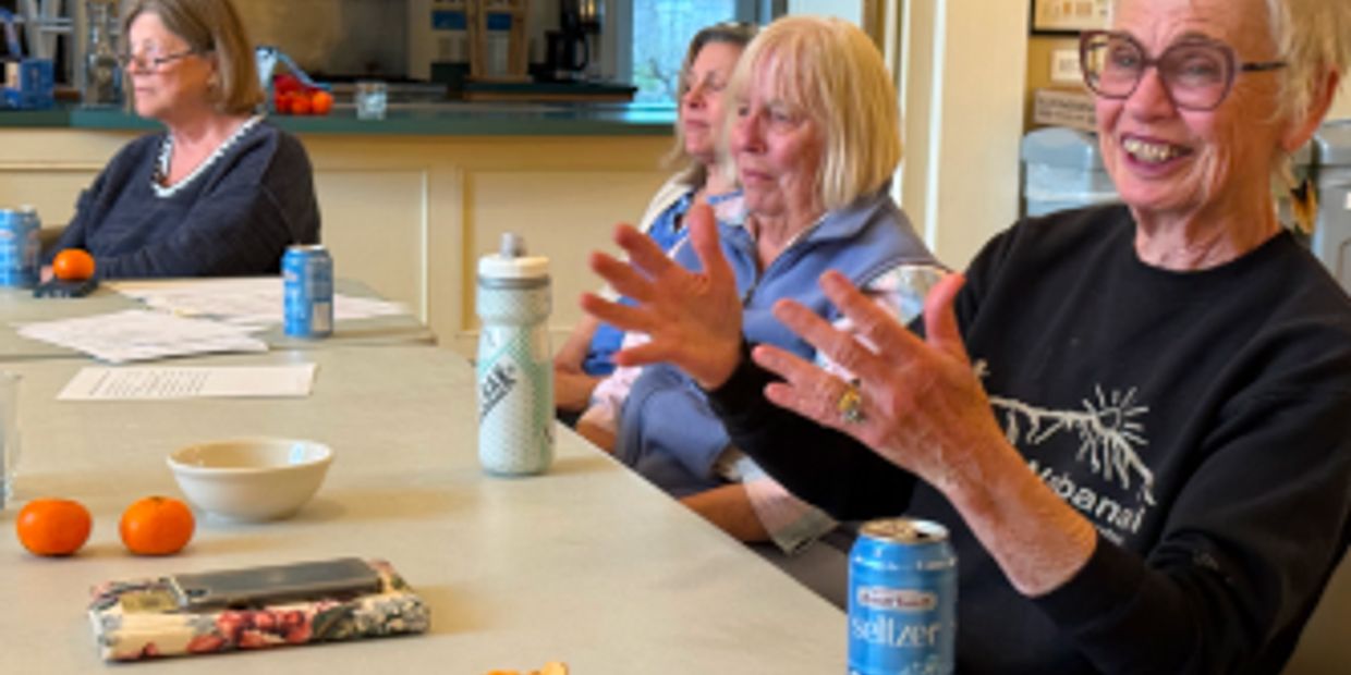 Four women sitting around a table, engaged in conversation with drinks and snacks.