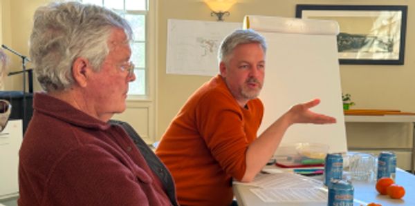Two men engaged in a discussion at a meeting table with documents and drinks.