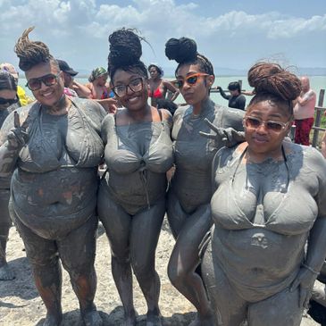 Four women covered in mud posing happily at a beach.