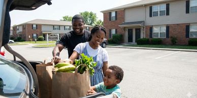 Happy family unloading groceries from car in a sunny suburban neighborhood.