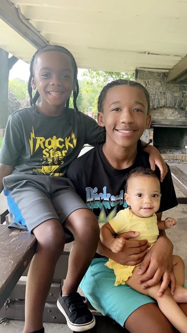 Three smiling children sitting together on a bench outdoors.