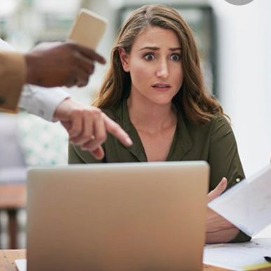 Worried woman looking at laptop with people pointing and showing phone.