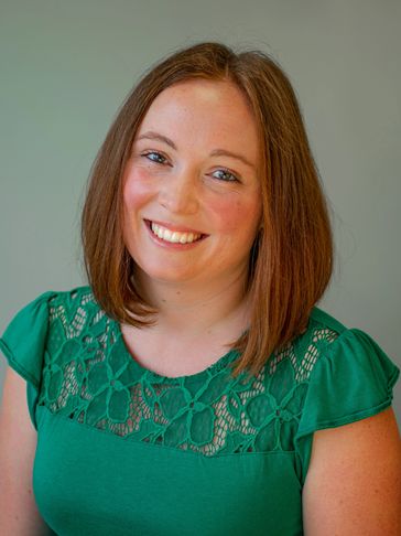 Smiling woman with shoulder-length brown hair wearing a green lace top.