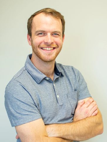 Smiling man in a gray polo shirt with arms crossed.