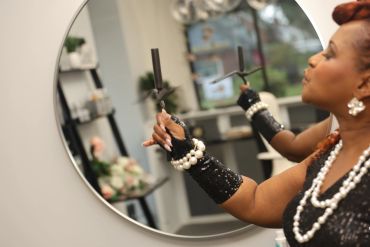 Woman stylishly holding black cigarettes near a round mirror.