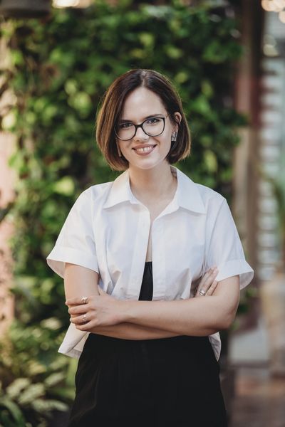 Smiling woman with glasses wearing a white shirt and black outfit outdoors.