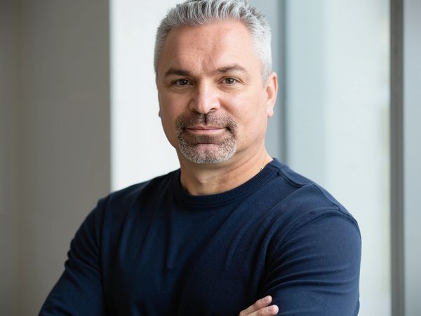 Confident man with arms crossed, wearing a dark shirt.