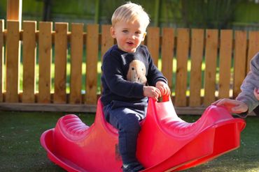A child at Kiwi Kids Preschool playing on a plastic rocking horse