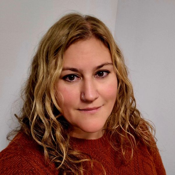 Woman with curly blonde hair wearing a rust-colored sweater.