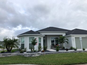 Modern single-story house with grey roof and well-maintained garden under a cloudy sky.