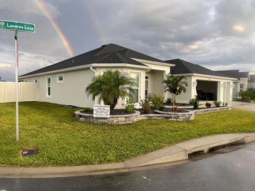 Double rainbow over a suburban house with landscaped garden beds.