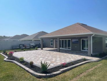 Modern backyard patio with tiled flooring and garden beds under clear blue sky.
