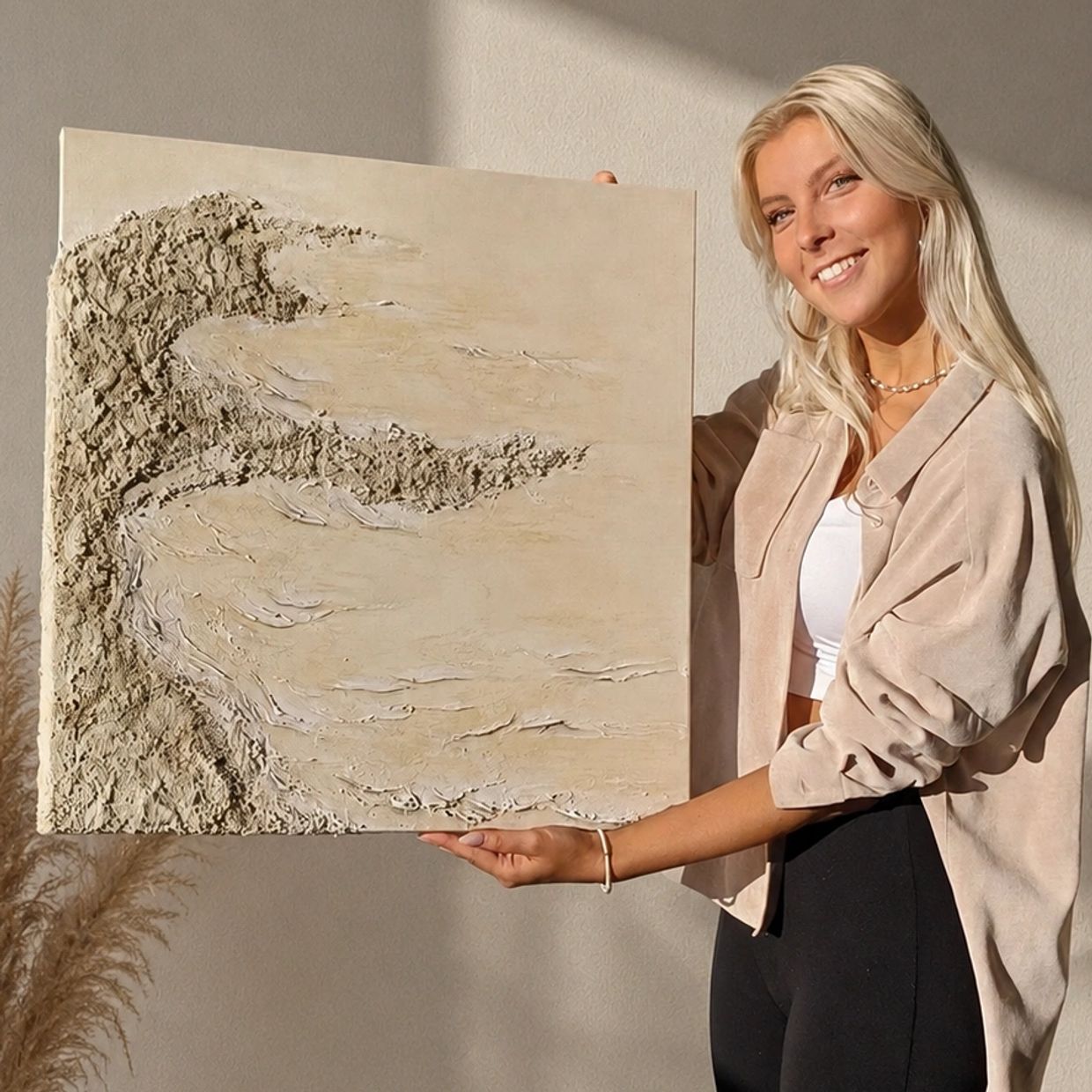 Woman proudly displays textured abstract painting with neutral tones.