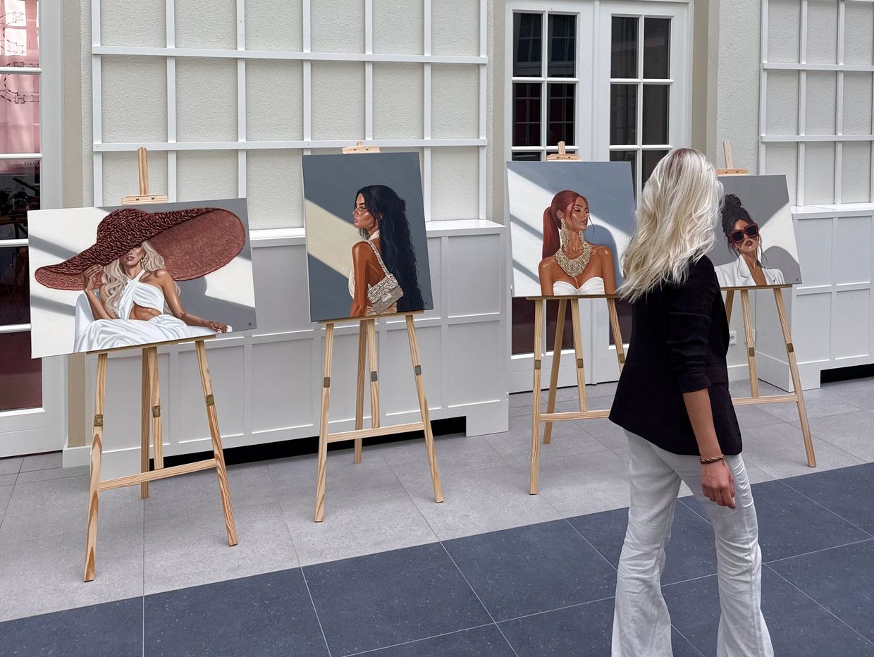 A woman viewing four stylish portrait paintings on easels indoors.