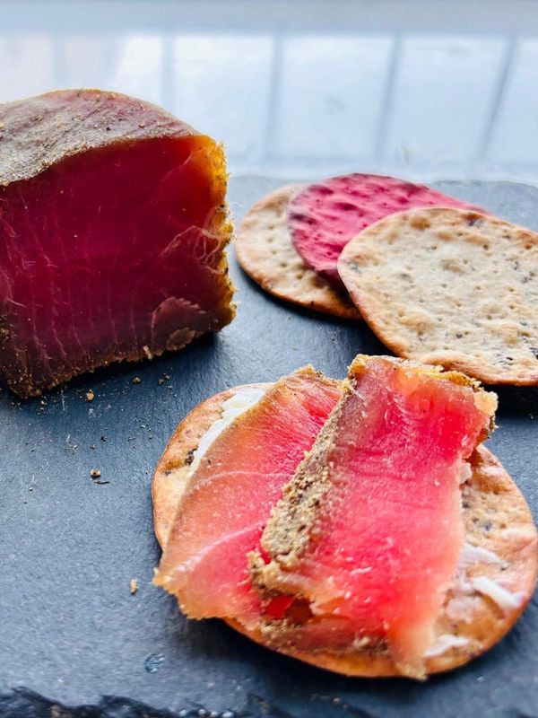 Slices of cured meat and crackers on a dark slate board.