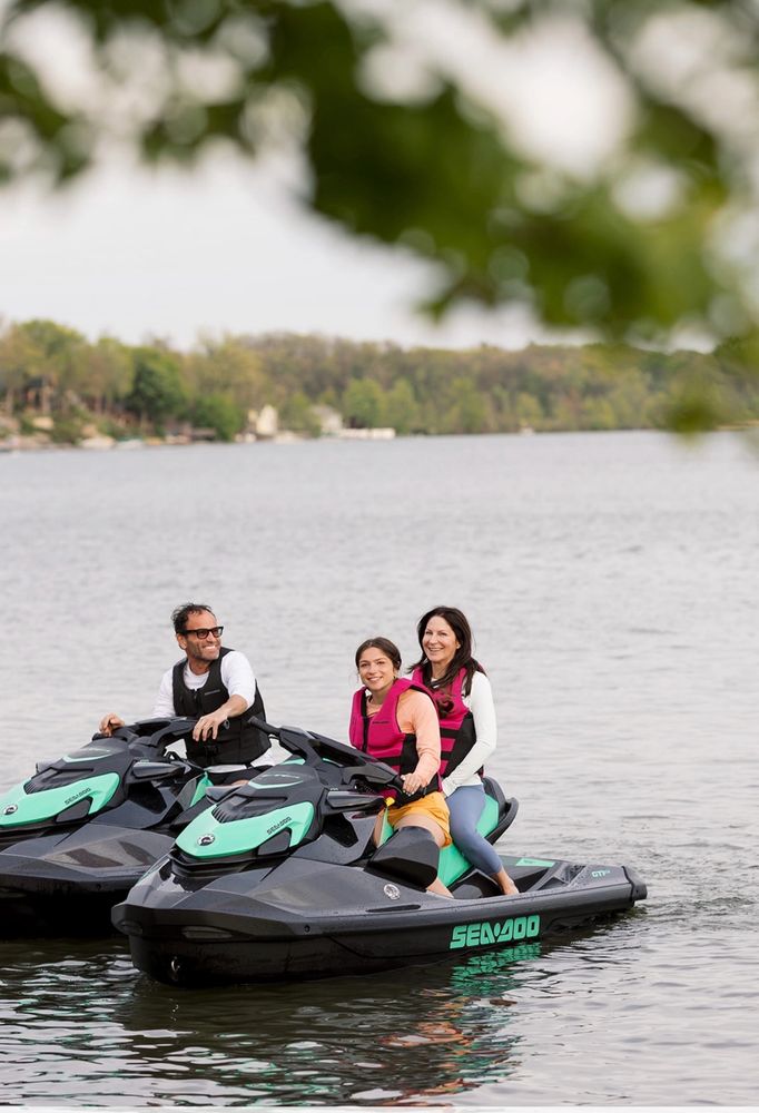 Three people enjoying a ride on Sea-Doo jet skis on a calm lake.