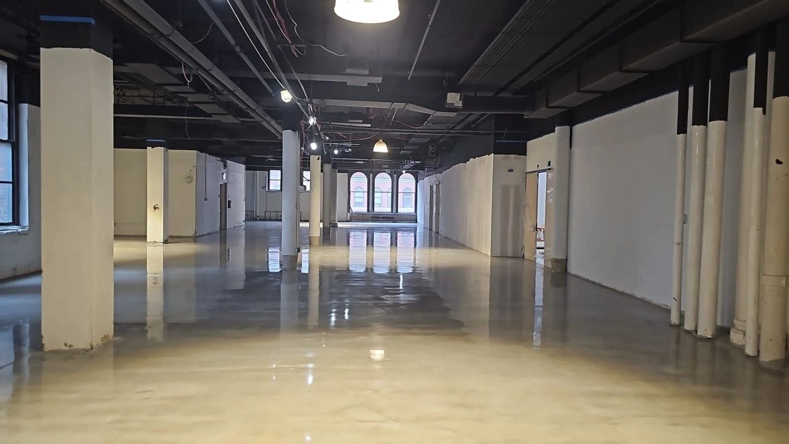 Empty industrial space with polished concrete floors and white pillars.