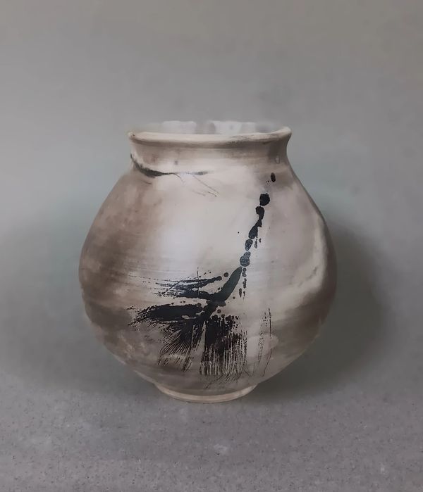 A rustic ceramic pot with black abstract brush strokes on a beige background.