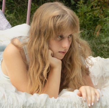 A thoughtful young woman lying on a bed outdoors.