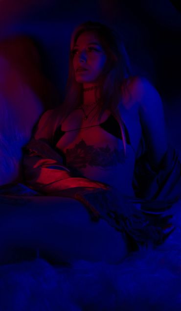 Woman sitting in dim, colorful lighting.