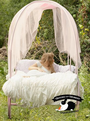 Girl lying on a bed under a canopy in a garden.