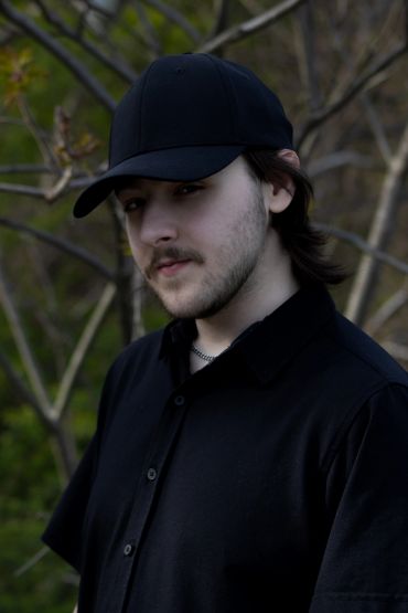Young man wearing a black cap and shirt outdoors.