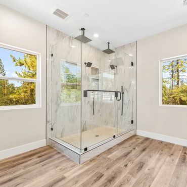 Modern glass shower enclosure with marble walls and wood-style flooring.