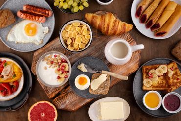 A diverse breakfast spread with eggs, sausages, croissant, fruits, and spreads.