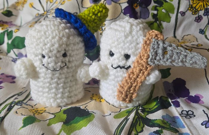 Two crocheted ghost figures, one with a green and blue hat, the other holding a crocheted axe.