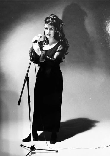 Woman in a long black dress singing into a microphone on stage.