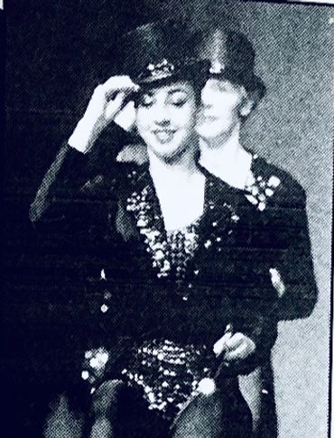 Two performers in sequined costumes and hats, one adjusting her hat.