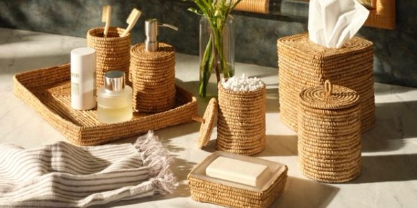 Woven bathroom accessories set on a marble surface with sunlight.
