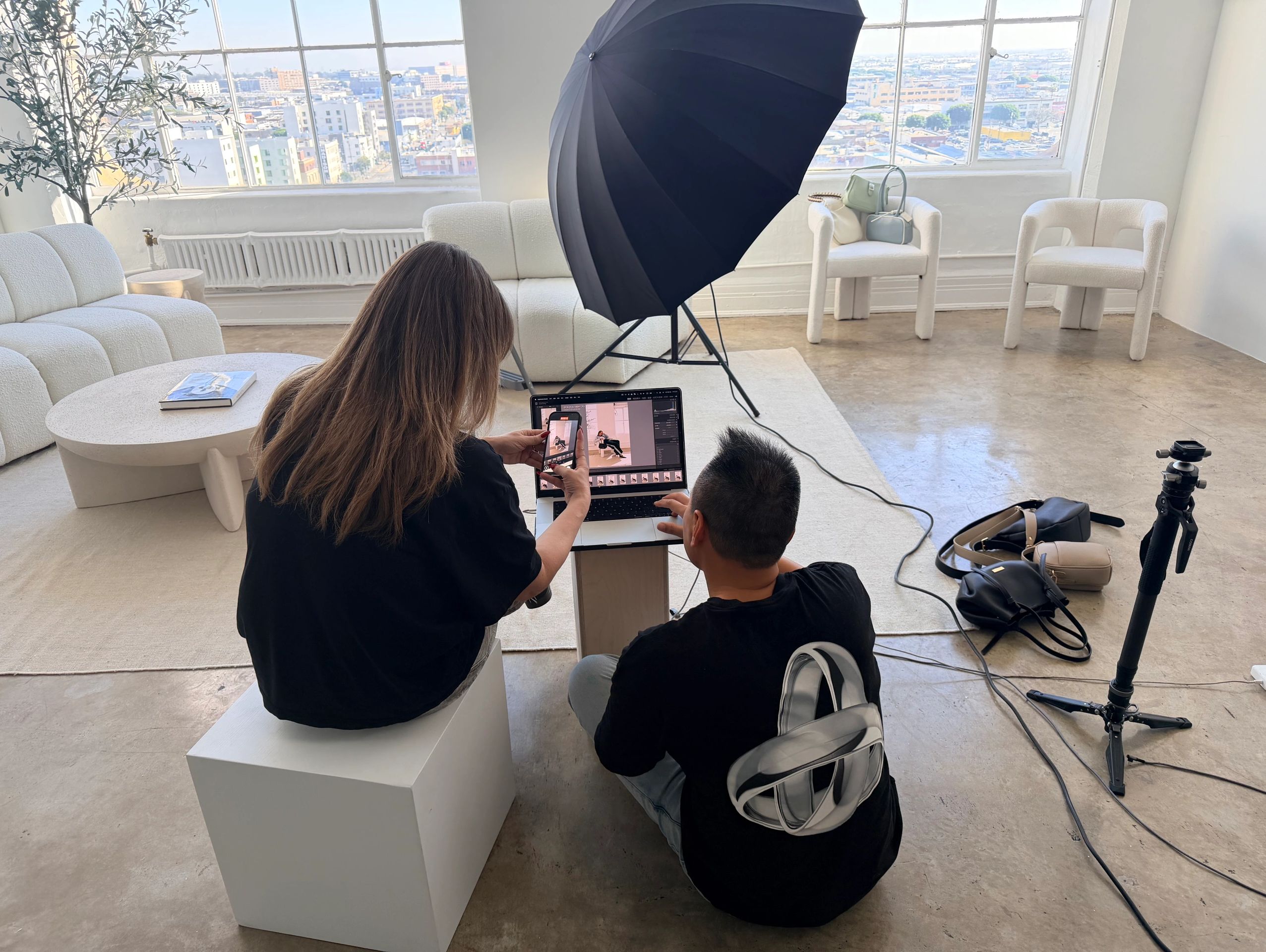 Two people reviewing photos on a laptop in a bright, modern studio with photography equipment.