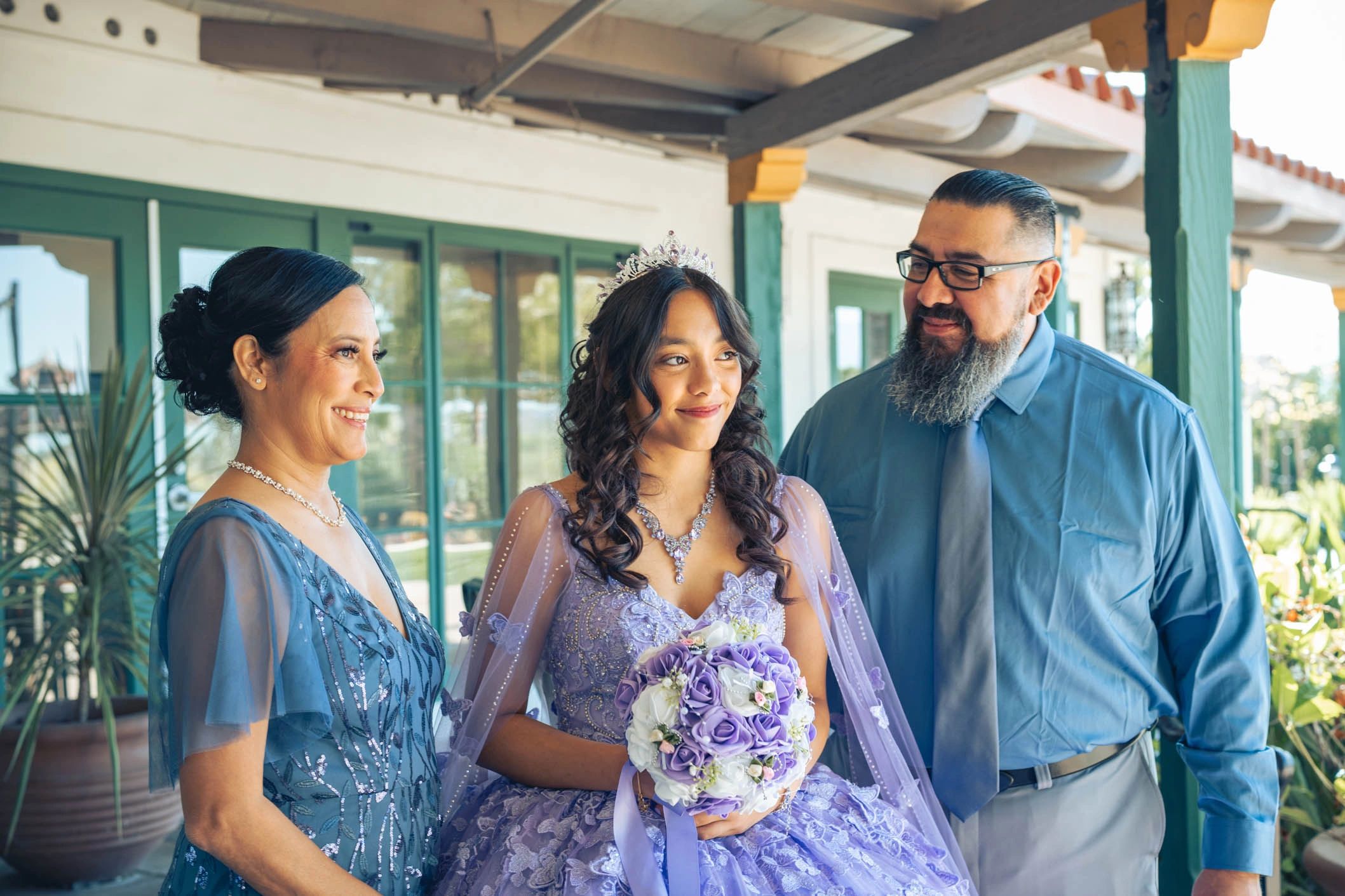 A young woman in a purple dress with her parents smiling beside her.
