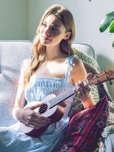 Young woman playing ukulele on a cozy couch with sunlight.