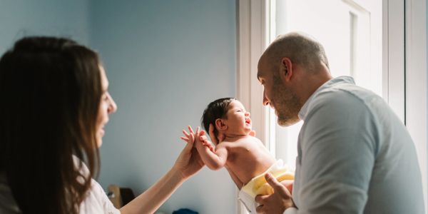 Parents joyfully holding and playing with their newborn baby by the window.