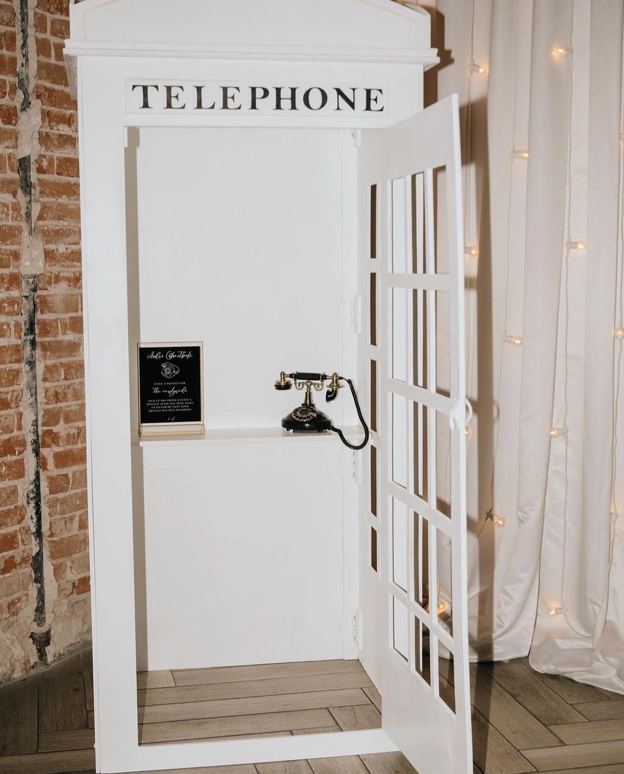 Vintage telephone booth with black rotary phone and sign inside.