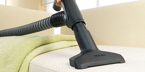 Vacuum cleaner cleaning a mattress in a bright room.