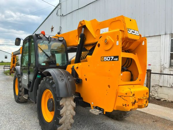 Yellow JCB 507-42 telehandler parked near a barn.
