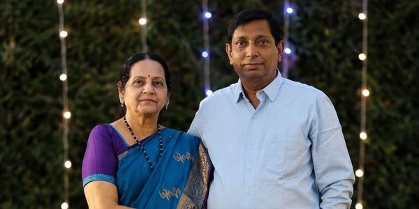 Smiling elderly couple posing outdoors with lights in background.