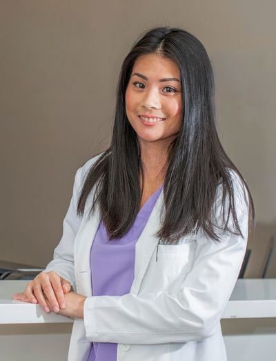 Smiling female doctor in a white coat and purple scrubs.