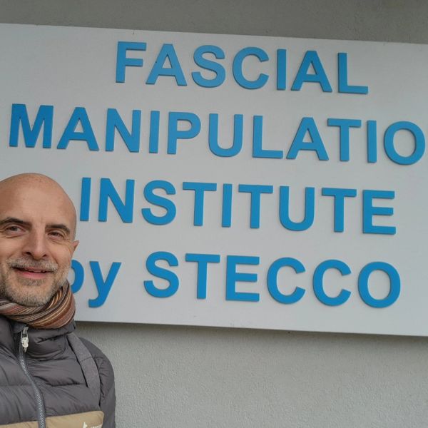 Man smiling in front of Fascial Manipulation Institute sign.