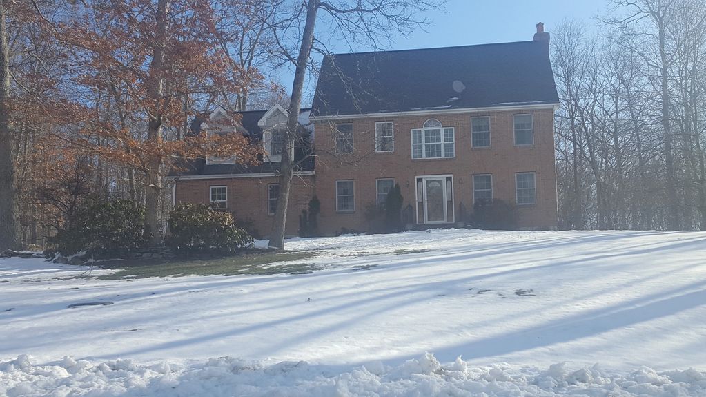Large brick house with snow-covered yard and bare trees in winter.