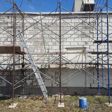 Scaffolding set up, wall is power washed, all bad mortar joints are ground out & deteriorated block